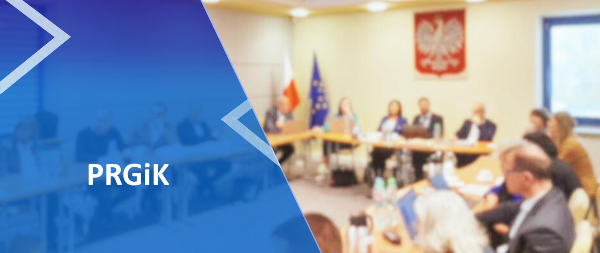 Po lewej stronie na niebieskim tle napis PRGiK, w tle rozmyte zdjęcie z posiedzenia Państwowej Rady Geodezyjnej i Kartograficznej